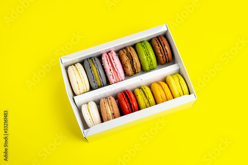 colorful macaroons in gift box for celebration romantic party birthday on yellow  pion flowers  satin ribbon top view  many different types flavors of macarons hand drawn decorated golden silver