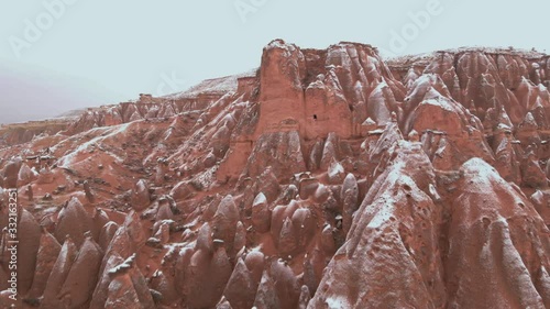 Cinematic aerial view of snowy landscape at Devrent Valley in Cappadocia. Fairy chimneys surronded by snow in Imaginary valley full of unique tuff rock formations in winter season in Cappadocia.  photo