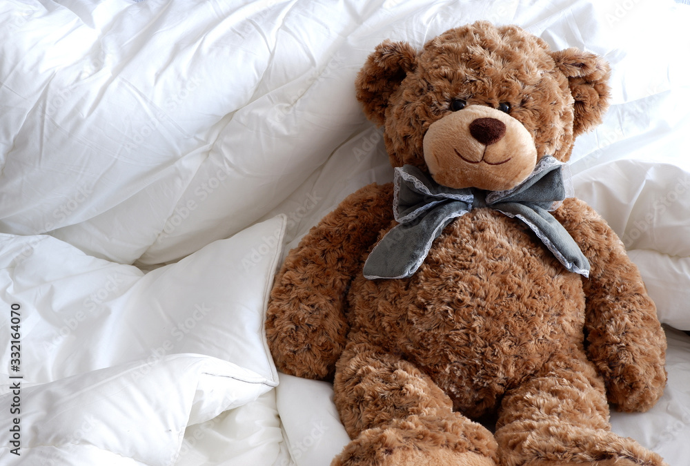 Soft toy brown bear sitting on the white bed linen.