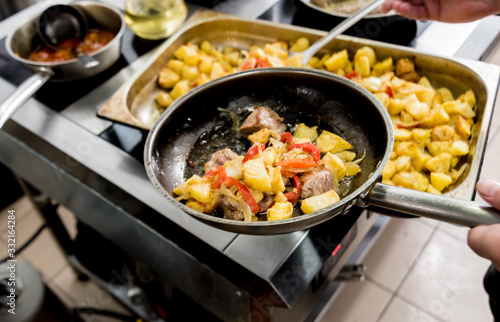 Chef cooks fried potatoes with pieces of meat in a restaurant kitchen