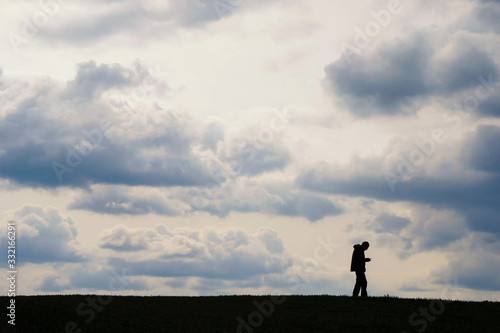 Silhouette of a man with a phone on a hill on a background of clouds in Ukraine. Information transfer concept. © Ganna Zelinska