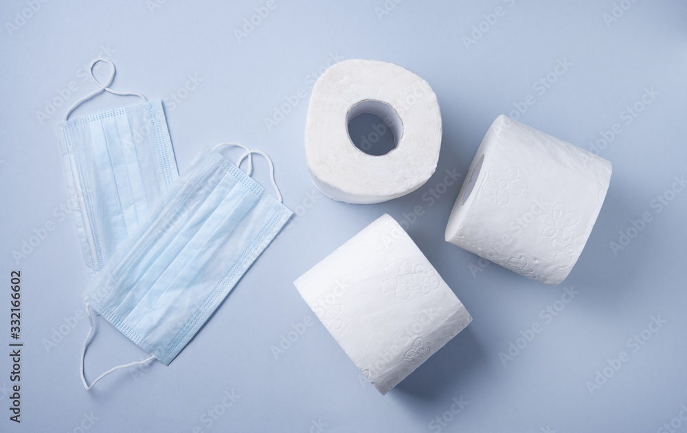 Obraz premium three rolls of white toilet paper and face masks on a blue background. Pandemic, covid-19, essential goods, scarcity