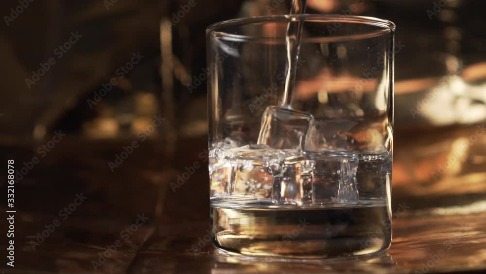 Pure mineral water is poured into a glass with ice cubes on a golden texture background close-up. slow motion Pure mineral water is poured into a glass with ice cubes on a golden texture background close-up. slow motion