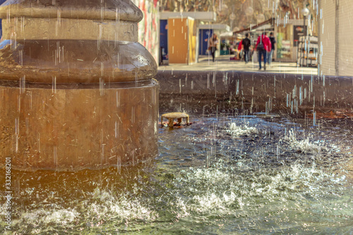 Fountain with water in the foreground, with street market background out of focus. Palma de Mallorca, island of Mallorca, Spain