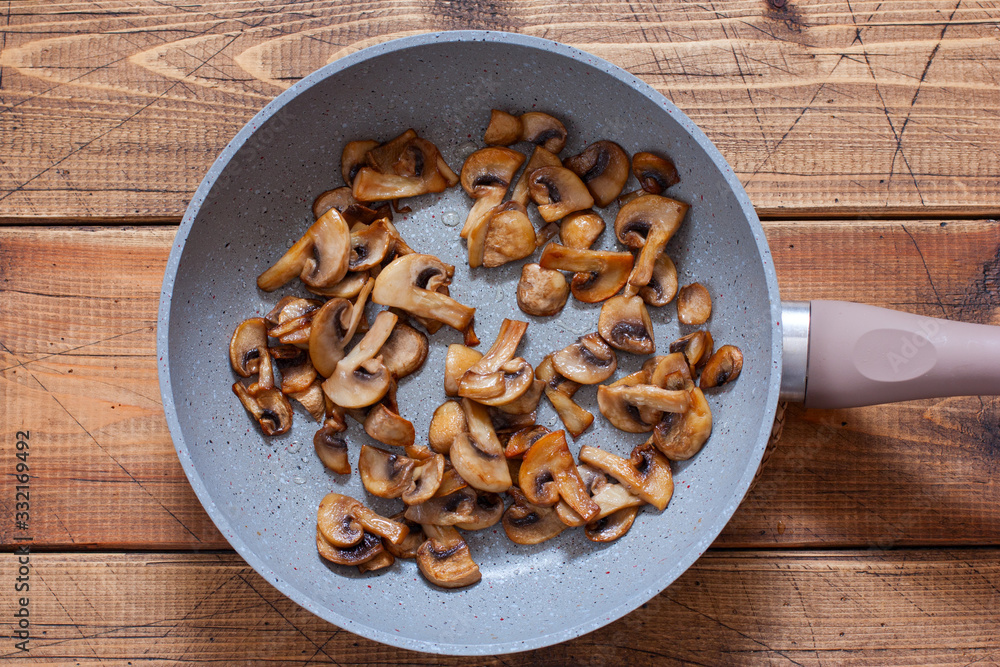 Fototapeta premium Step-by-step preparation of risotto with mushrooms and chicken breast, step 2 - frying chopped champignons, top view, selective focus