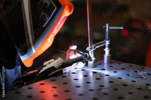 A tig welder works in a workshop and welds a metal pipe