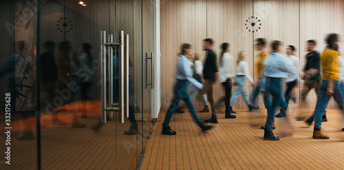 Group of office employees in motion go around at coworking space. People in business center walking  at hall. Motion blur. Wide image