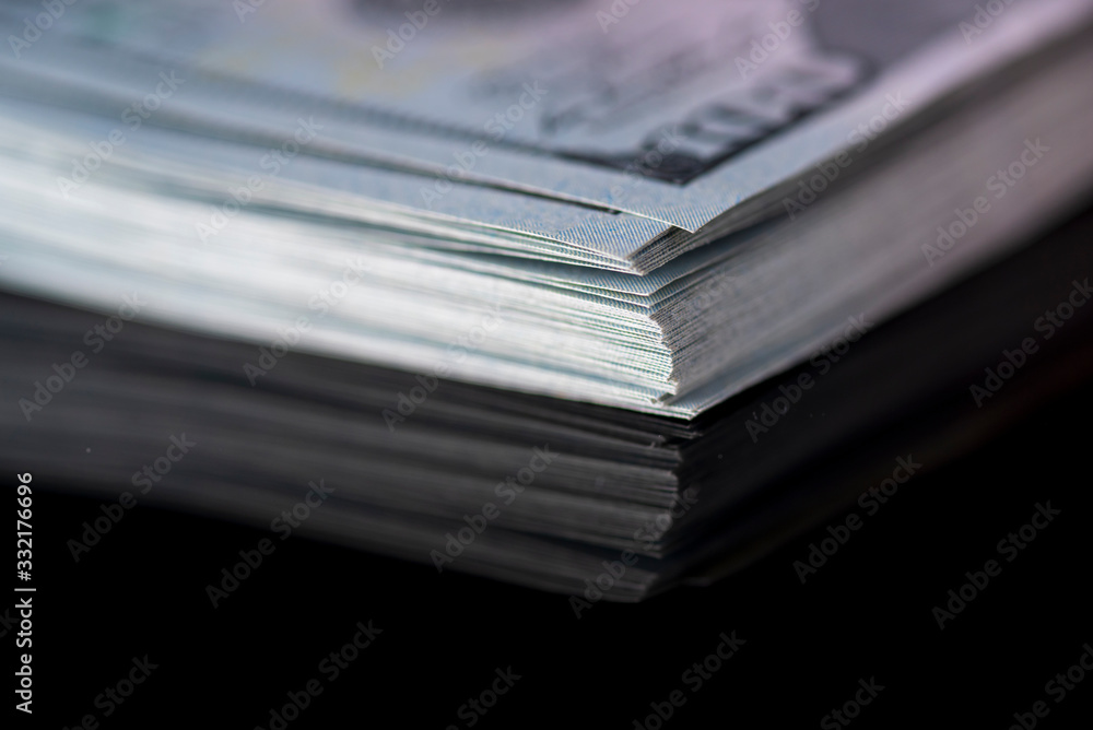 A stack of hundred dollar bills against a dark background. Photographed close-up. A stack of hundred dollar bills against a dark background. Photographed close-up.