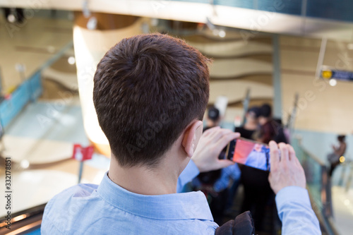 A man with a phone is traveling on an escalator in a subway. A man takes off the passengers of the subway on his smartphone going down the escalator.