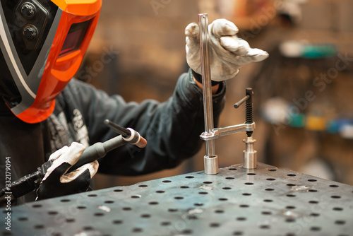 A welder works in a workshop and welds by tig a custom clamp