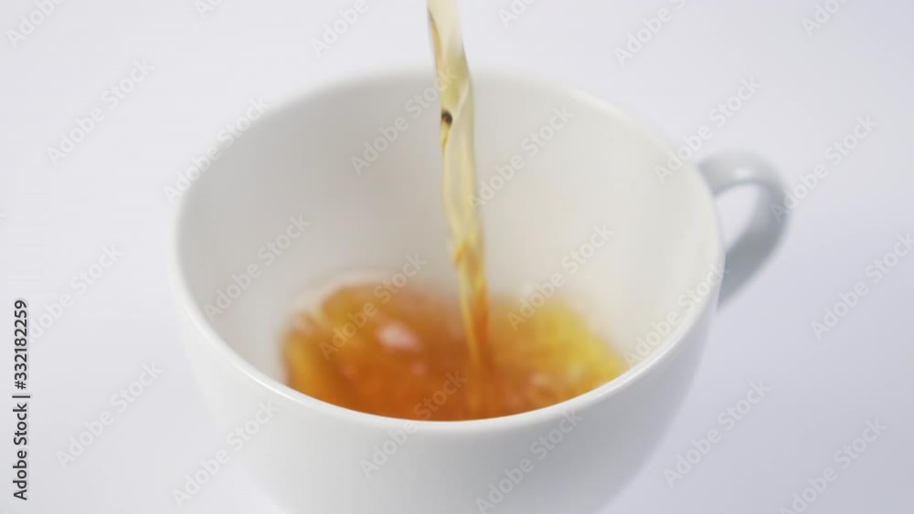 Black tea is pouring into a white cup on the table. Slow motion. Macro shot. Black tea is pouring into a white cup on the table. Slow motion. Macro shot.