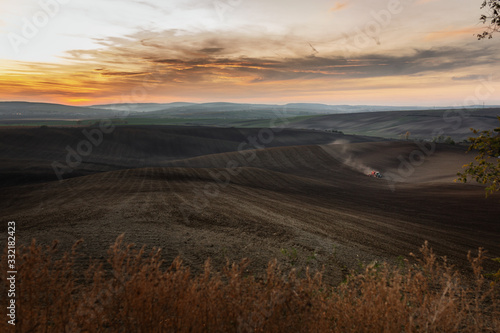 An epic panorama of Moravian fields with the setting sun where a farmer works hard with in tractor © Piotr