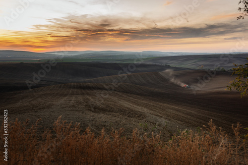 An epic panorama of Moravian fields with the setting sun where a farmer works hard with in tractor