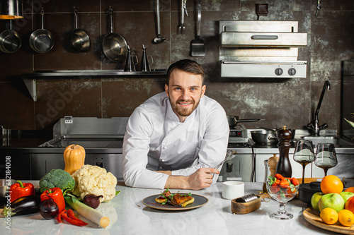 portrait of good-looking smiling cook man in the kitchen, looking at camera. posing with delicious dish