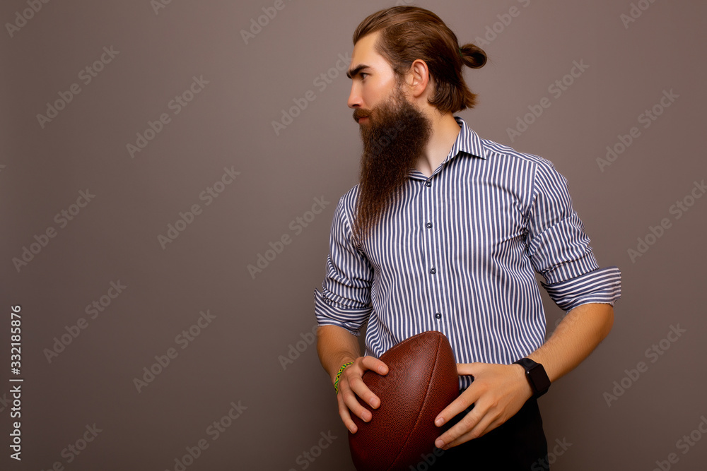Serious businessman in formal wear with rugby ball isolated on grey background with copy space. Portrait of bearded stylish man holds a game ball in his hands.