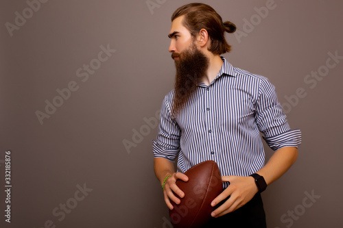 Serious businessman in formal wear with rugby ball isolated on grey background with copy space. Portrait of bearded stylish man holds a game ball in his hands. 