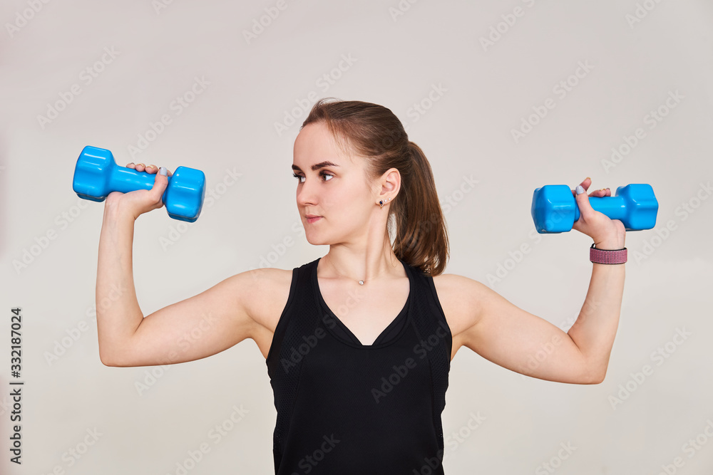 young woman performs an exercise with dumbbells looking to the side, half-length portrait on a light background young woman performs an exercise with dumbbells looking to the side, half-length portrait on a light background