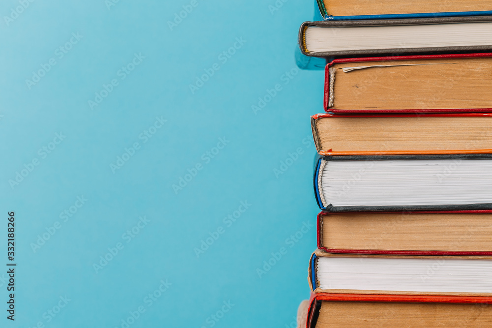 A simple composition of many hardback books, raw books on a wooden table and a bright blue background. Going back to school. Copy space. Education. A simple composition of many hardback books, raw books on a wooden table and a bright blue background. Going back to school. Copy space. Education.