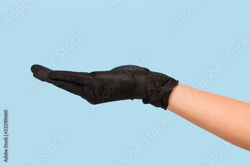 hand in a black medical glove holds an object on a blue background. Mock up, you can insert your product for advertising