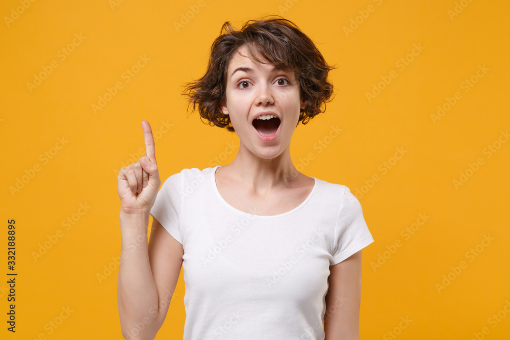 Excited young brunette woman girl in white t-shirt posing isolated on yellow orange background studio portrait. People lifestyle concept. Mock up copy space. Hold index finger up with great new idea. Excited young brunette woman girl in white t-shirt posing isolated on yellow orange background studio portrait. People lifestyle concept. Mock up copy space. Hold index finger up with great new idea.