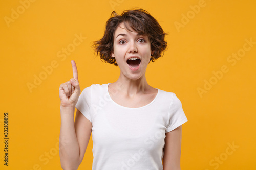 Excited young brunette woman girl in white t-shirt posing isolated on yellow orange background studio portrait. People lifestyle concept. Mock up copy space. Hold index finger up with great new idea.