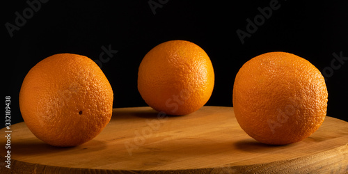 Three oranges on a wooden table on a dark background