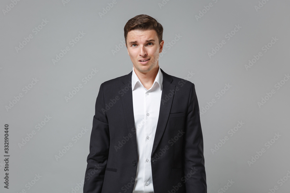 Perplexed shocked young business man in classic black suit shirt posing isolated on grey background studio portrait. Achievement career wealth business concept. Mock up copy space. Looking camera. Perplexed shocked young business man in classic black suit shirt posing isolated on grey background studio portrait. Achievement career wealth business concept. Mock up copy space. Looking camera.