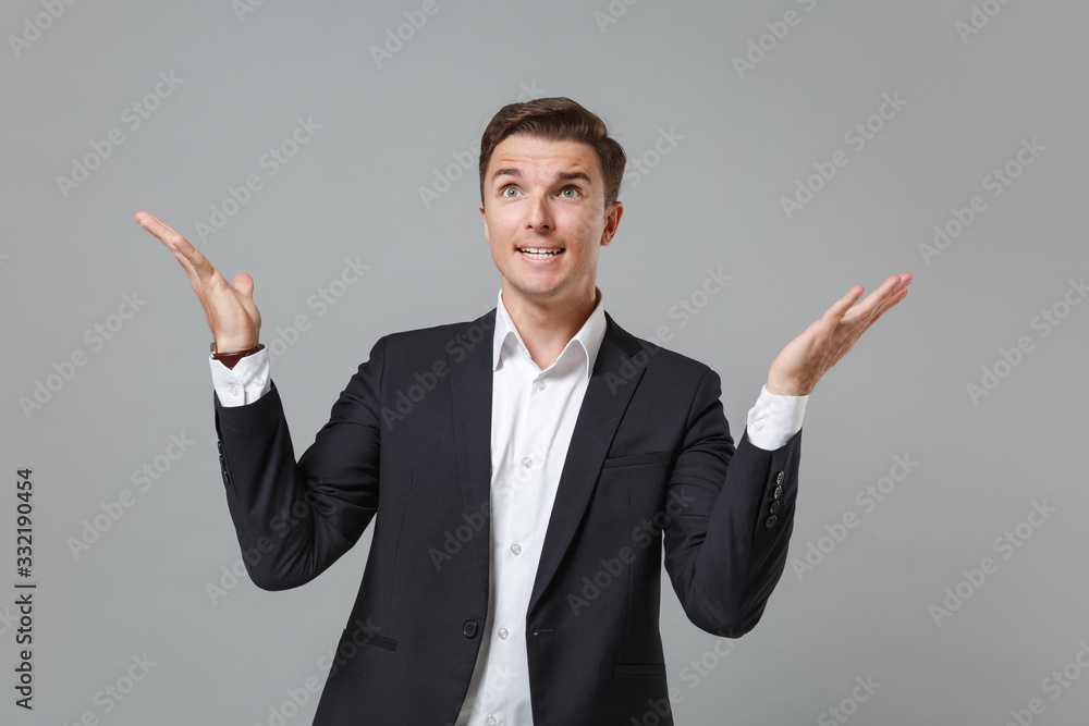 Nervous perplexed young business man in classic black suit shirt posing isolated on grey background studio portrait. Achievement career wealth business concept. Mock up copy space. Spreading hands. Nervous perplexed young business man in classic black suit shirt posing isolated on grey background studio portrait. Achievement career wealth business concept. Mock up copy space. Spreading hands.