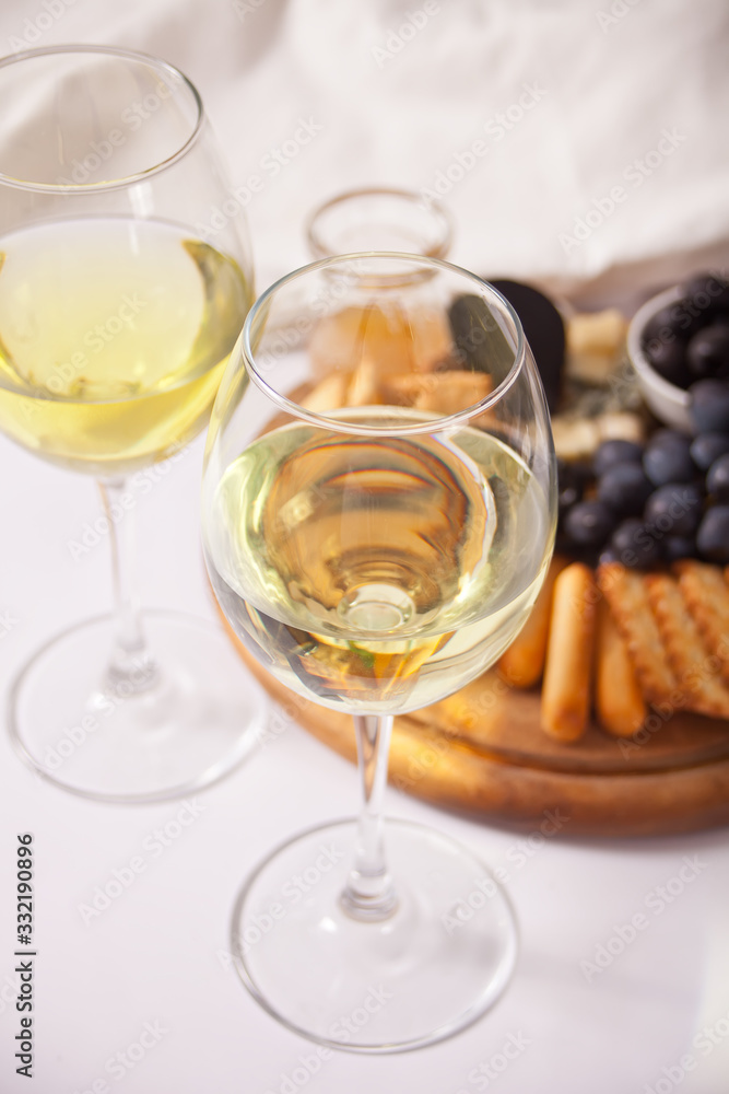Two glasses of white wine and plate with assorted cheese, fruit and other snacks for party