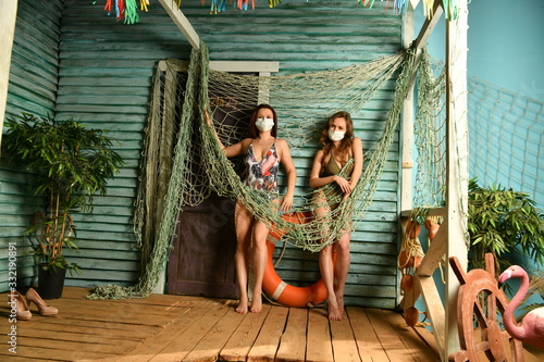 two girls in swimsuits and medical bandages with a lifebuoy on the porch of a fishing house