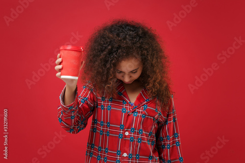 Tired young african american girl in pajamas homewear posing resting at home isolated on red background. Relax good mood lifestyle concept. Hold paper cup of coffee or tea yawning with lowered head.