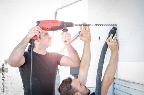zwei freundliche Handwerker bohren mit der Bohrmaschine in die Hauswand um später eine Markise zu befestigen photo