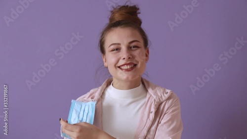 Beautiful girl standing isolated over lilac background taking off medical mask, wants to avoid coronovirus, takes a few breaths of fresh air. Global covid-19 pandemic, coronavirus, panic concept photo