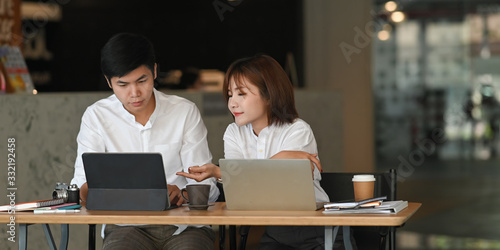 Cropped image of business developer team discussing/planning/meeting by using a computer tablet and laptop while sitting together at the wooden meeting table over modern office as background.