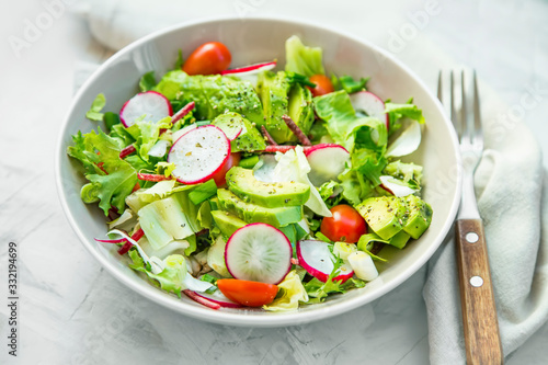 Fresh vegetable salad bowl closeup, healthy organic vegetables salad with radish, spinach, tomatoes, onion, avocado