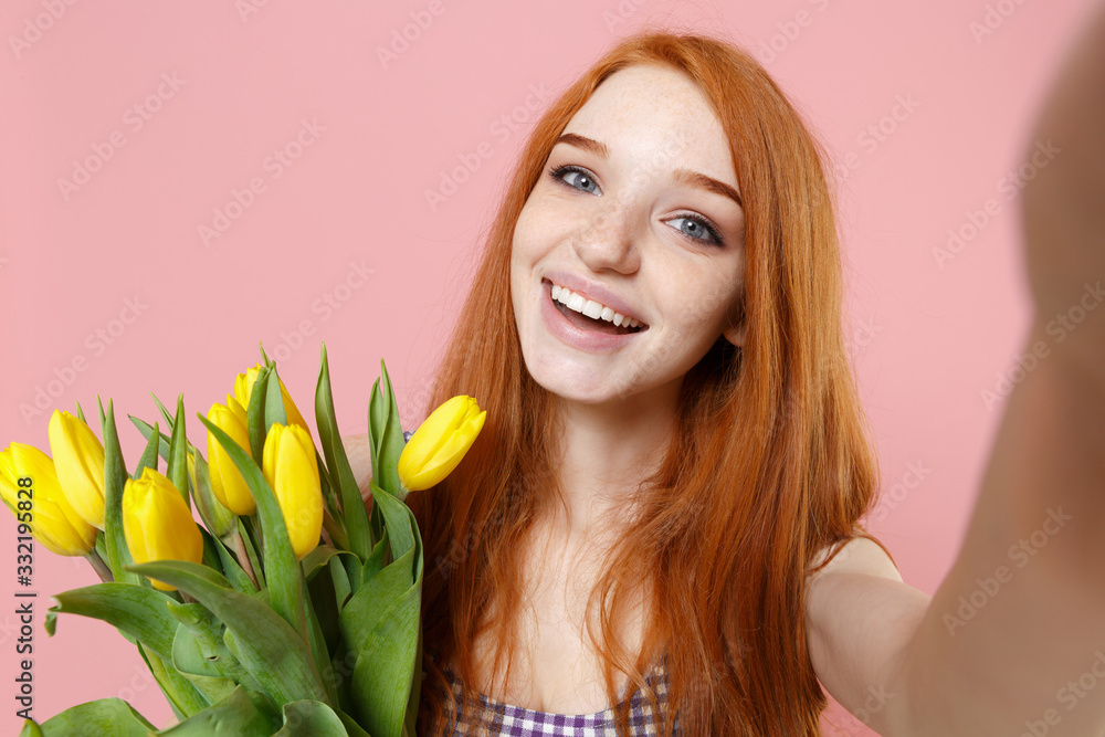 Close up of funny redhead woman girl in plaid dress isolated on pastel pink background. People lifestyle concept. Mock up copy space. Hold bouquet of yellow tulips doing selfie shot on mobile phone. Close up of funny redhead woman girl in plaid dress isolated on pastel pink background. People lifestyle concept. Mock up copy space. Hold bouquet of yellow tulips doing selfie shot on mobile phone.