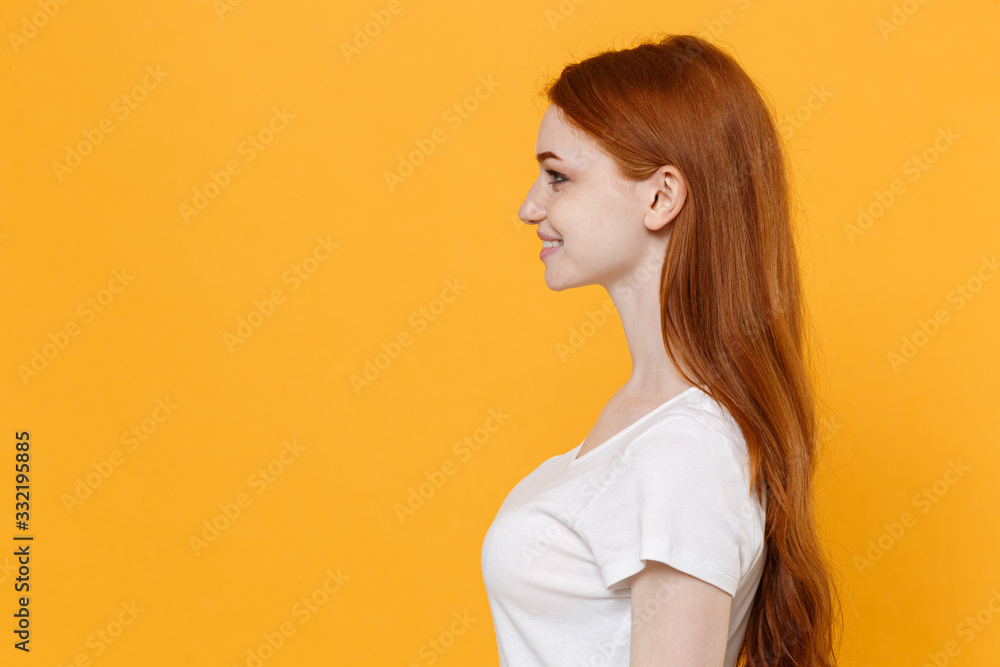 Side view of smiling young redhead woman girl in white blank empty t-shirt posing isolated on yellow background studio portrait. People emotions lifestyle concept. Mock up copy space. Looking aside. Side view of smiling young redhead woman girl in white blank empty t-shirt posing isolated on yellow background studio portrait. People emotions lifestyle concept. Mock up copy space. Looking aside.