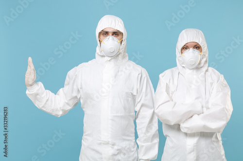 Two people in protective suits respirator masks isolated on blue background studio. Epidemic pandemic new rapidly spreading coronavirus 2019-ncov originating in Wuhan China, virus concept stop gesture