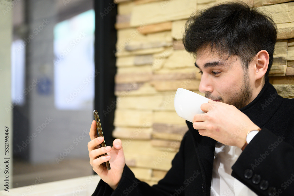 Portrait smiling and happy man playing mobile phone.Handsome business young man sitting on chair and drinking coffee in the restaurant. Portrait smiling and happy man playing mobile phone.Handsome business young man sitting on chair and drinking coffee in the restaurant.