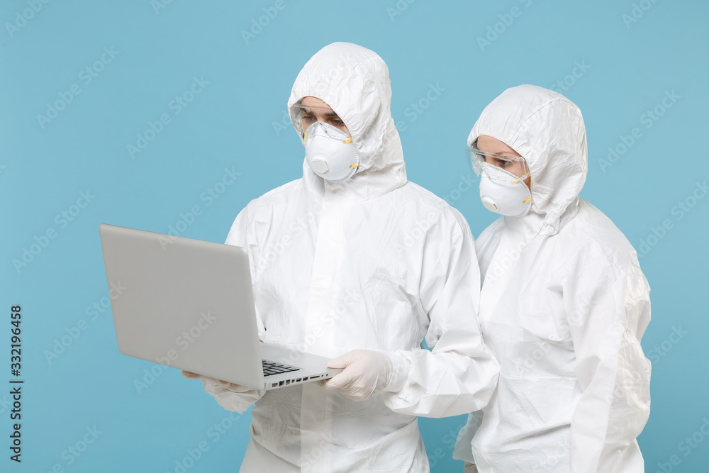 People in protective suits respirator masks hold work on laptop pc computer isolated on blue background studio. Epidemic pandemic new rapidly spreading coronavirus 2019-ncov medicine flu virus concept People in protective suits respirator masks hold work on laptop pc computer isolated on blue background studio. Epidemic pandemic new rapidly spreading coronavirus 2019-ncov medicine flu virus concept