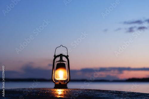 Old rusty lantern on the wet rock. Beautiful sunset sky and sea on background. Kerosene lamp soft glow at the seaside.
