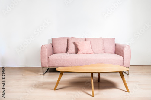 A pink sofa with metal frame and an oak coffee table in front of a white wall, over light hard wood floors. Copy space on the wall.