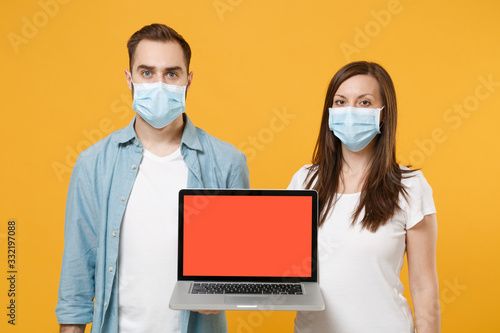 Two people in sterile face masks using laptop pc isolated on yellow background studio. Epidemic pandemic rapidly spreading coronavirus 2019-ncov medicine flu virus ill sick disease treatment concept.