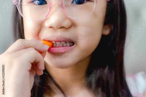 Child little girl eats vegetable salad using hand. Portrait of cheerful asian girl eating salad with joy. She is looking aside with curiosity and smiling.