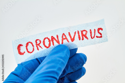 Hand in blue medical glove is holding inscription Coronavirus on white background.