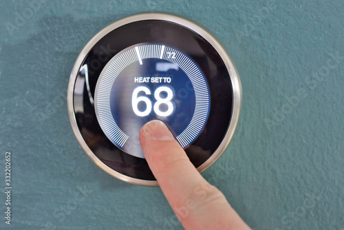 Hand adjusting the dial on nest smart home thermostat. Pressing center button to save money heating and cooling.
