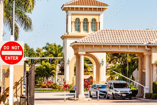A car enters a gated community after passing through a security guardhouse while a second car waits. A large Do Not Enter sign is also shown.