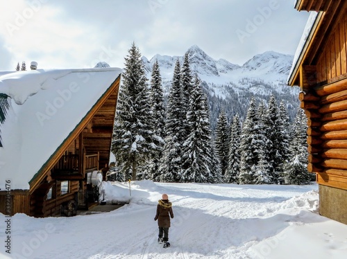 A young female snowshoer walking in between two wood cabins during the winter in the remote snow covered forests of Fernie, British Columbia, Canada. photo