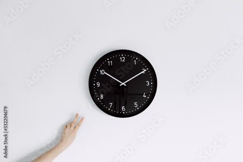  clock on white wall with one hand making peace gesture next to clock