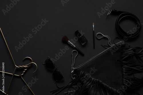 Black monochromatic flatlay composition on black background. Hangers, make-up brush, handbag, sunglasses, perfume, phone,nail polish, belt.Minimalist black, black friday.Top view, Copy Space Flat Lay.